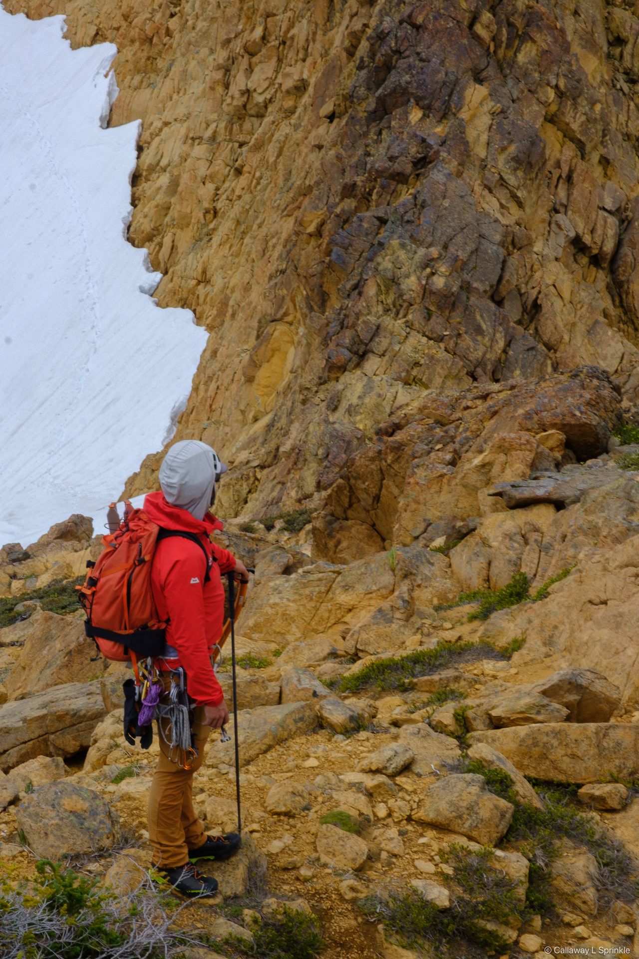 A climber in red seen from behind, downclimbing blocky orange rock