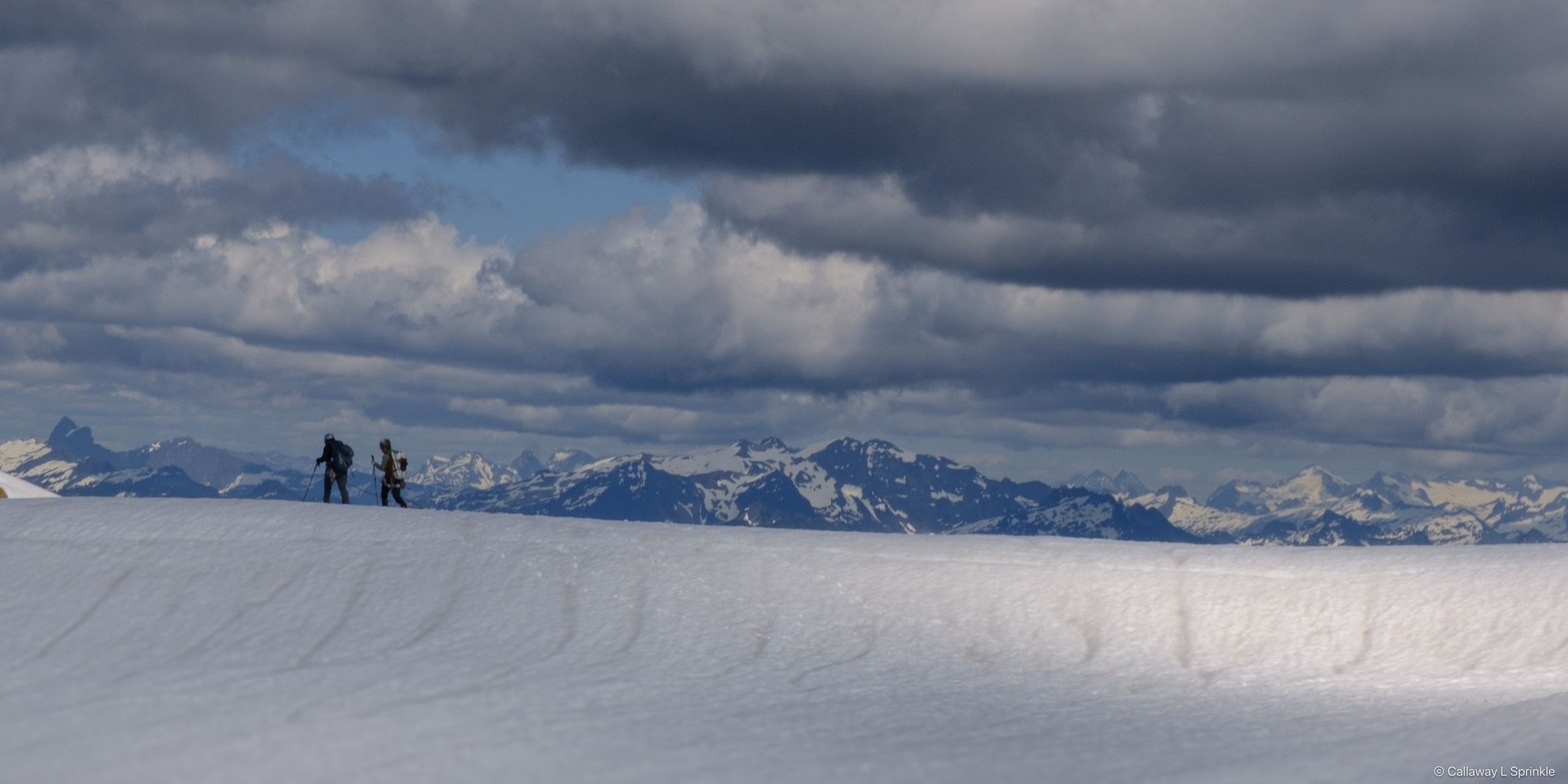 Three small figures crossing a broad flat glacier under a wide cloudy sky