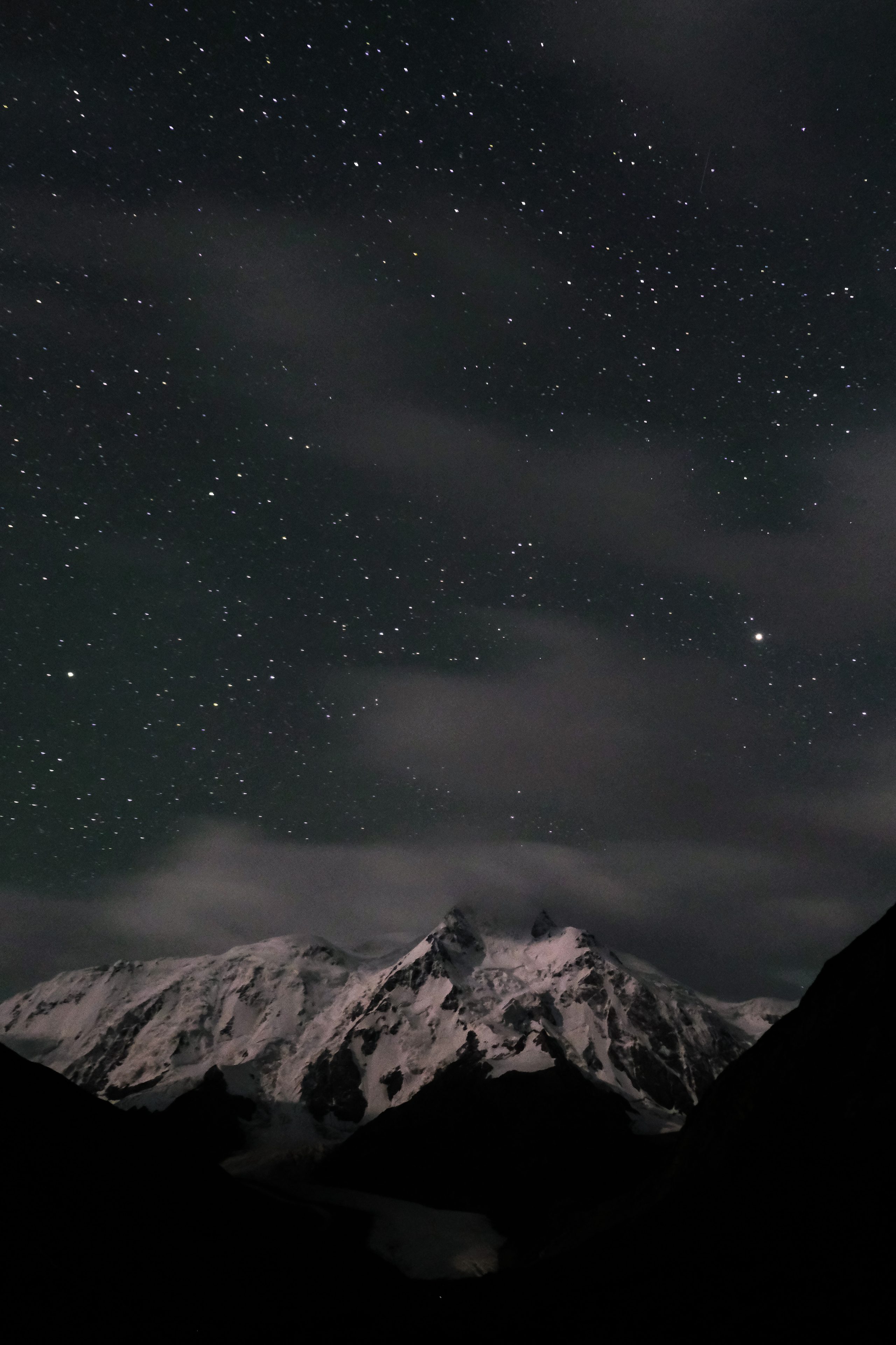 A starfield over a moonlit glaciated massif, thin cloud crossing the summits.